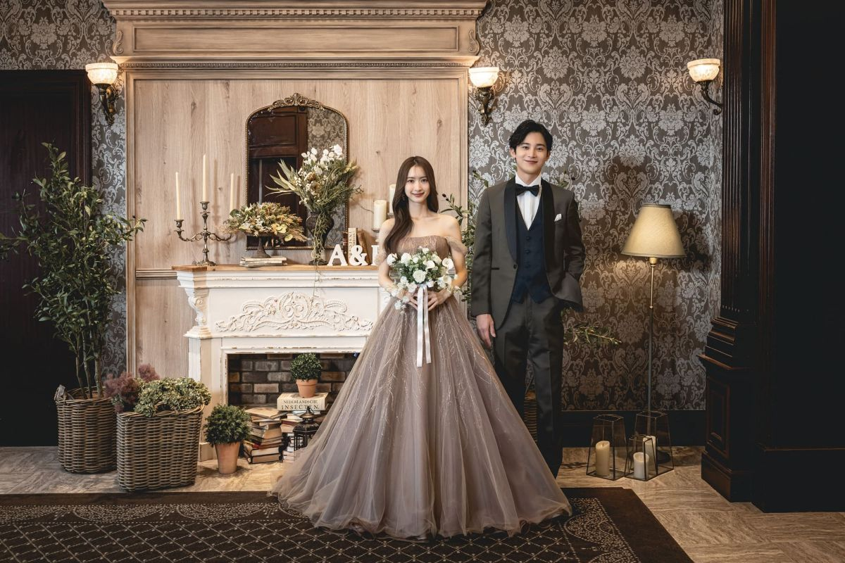 アンティーク調の室内で立つ、グレーのドレス姿の新婦とタキシード姿の新郎